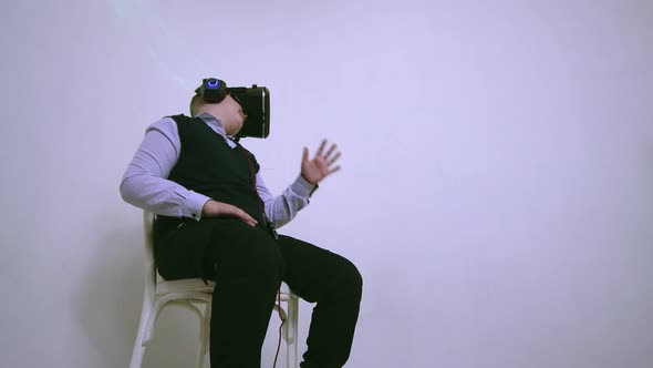 A Boy in Augmented Reality Glasses Sits on a Chair and Dances Cheerfully