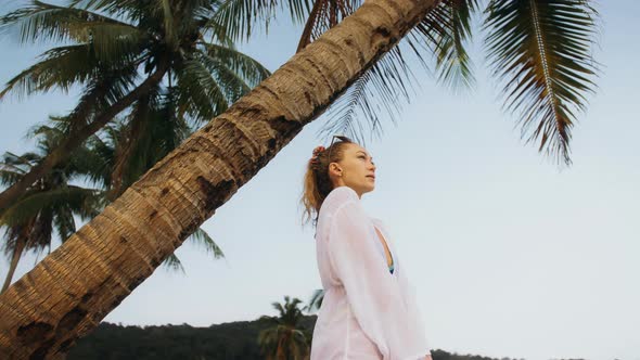 Woman in a White Tunic Shirt on Beach Near Stormy Sea Tilted Palm Tree