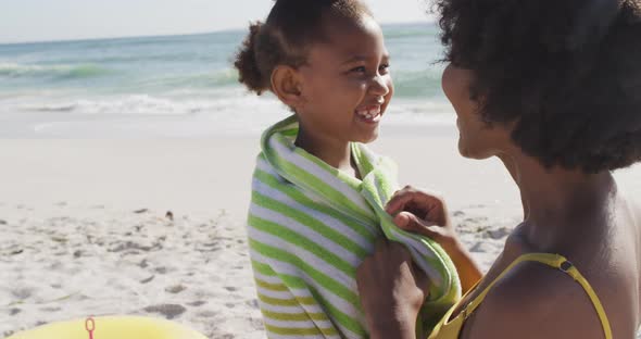 Smiling african american mother toweling off her daughter on sunny beach
