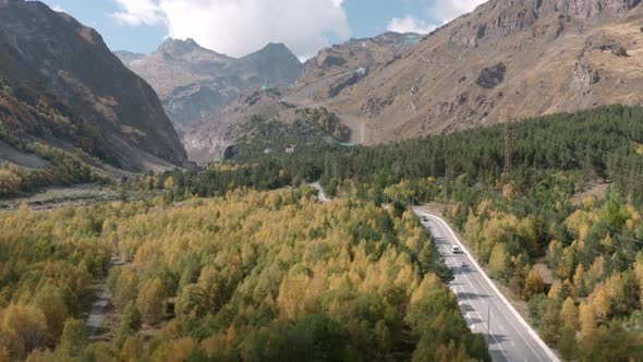 Car Road Through Autumn Forest To Mountain City. Aerial View Resort City on Mountain Foot. Tourist