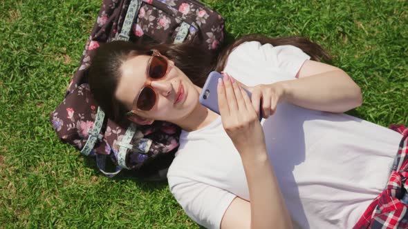 Top View of Happy Young Woman Lying Outdoors in Park Using Mobile Phone