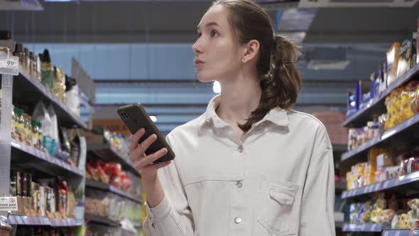 Young Woman Looking at a Smartphone Screen in a Supermarket