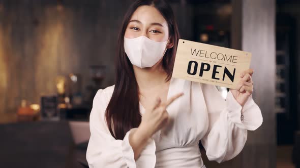 Business owner attractive young asian woman in apron hanging we're open sign