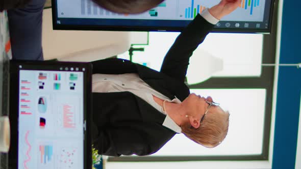 Elderly Project Manager Pointing at Desktop Presenting Statistical Data