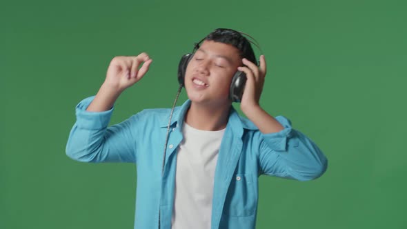 Young Asian Boy Listening To Music With Headphones And Dancing In The Green Screen Studio