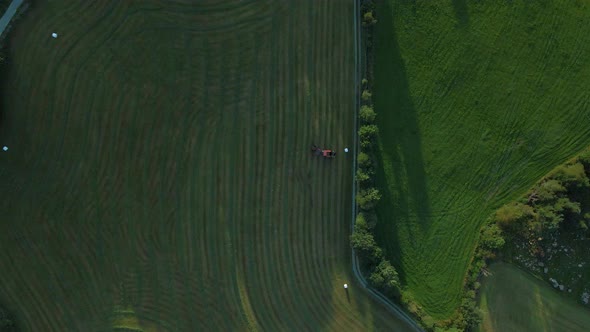 Aerial View Of A Baler Making Rolls Of Hay Bales On Green Farmland, Norway. top-down