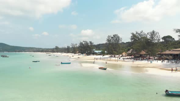 Populated shallow exotic shore with tourists and fishing boats in Saracen Bay in Koh Rong Sanloem