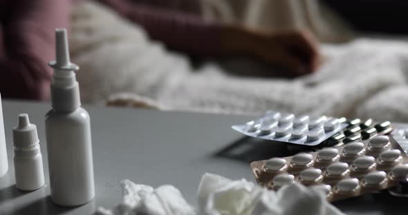 Sick young woman measuring temperature at home on the pills and tablets on the background