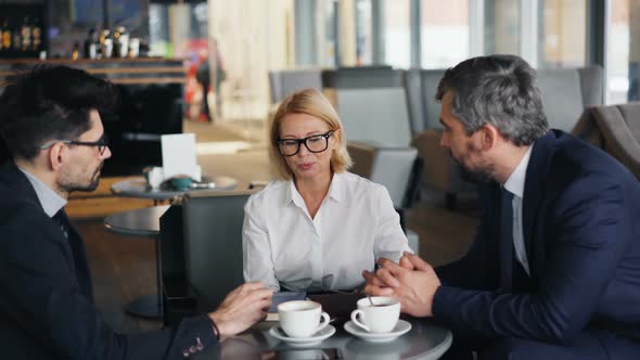 Cheerful Business Lady Negotiating Agreement with Male Partners Meeting in Cafe