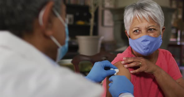 Male doctor visiting senior mixed race woman giving her vaccination