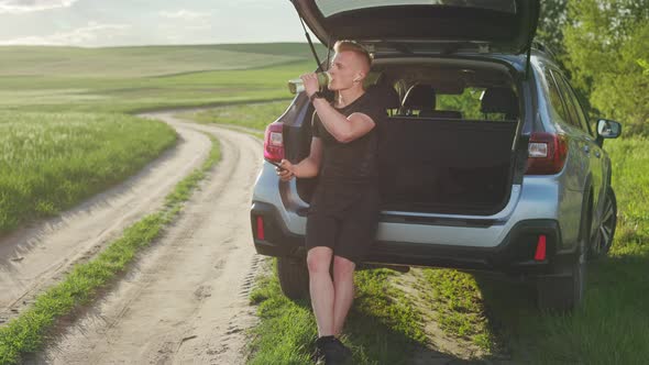 A Young Man in a Sports Uniform is Sitting in the Trunk of a Car