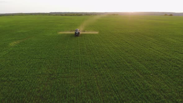 Aerial View of Farming Tractor Spraying on Field with Sprayer, Herbicides and Pesticides at Sunset