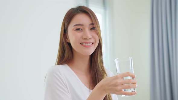 Asian attractive woman sit on bed, drink a glass of water after wake up in bedroom at home.