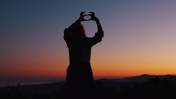 silhouette of girl making heart symbol with her hands