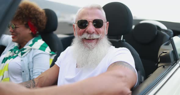 Senior multiracial couple inside a convertible car on holiday time