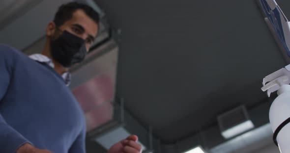 Businessman wearing face mask using sanitizer to disinfect hands as he enters the workplace