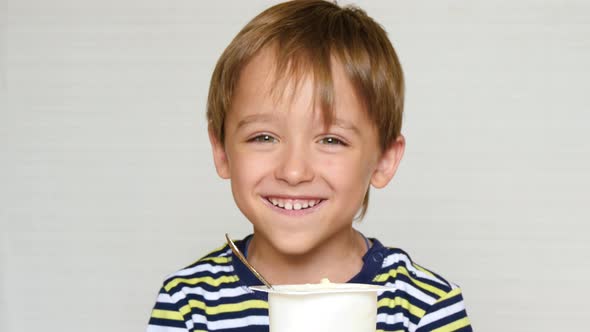 Portrait of a Laughing Boy. Happy Little Boy Eating Yogurt While Sitting at the Table