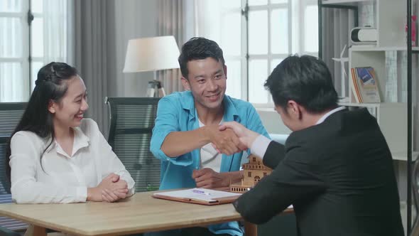 Asian Couple With A House Purchase Contract Paper Receives The Keys From A Real Estate Agent