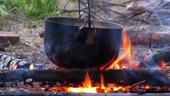 Cooking on an Open Fire in a Tourist Pot. Tourist Bowler Hat Hanging at Bonfire