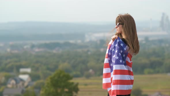 Young happy american woman with long hair holding waving on wind USA national flag on her