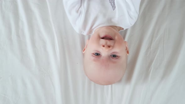upside down portrait of a cheerful toddler in white on the bed