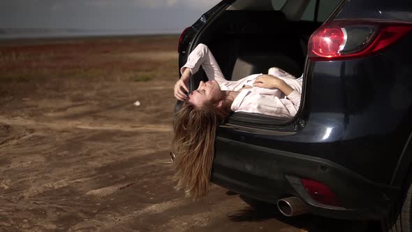 Portrait of a Long Haired Woman Traveler Having a Break Laying in Car Trunk and Relaxing