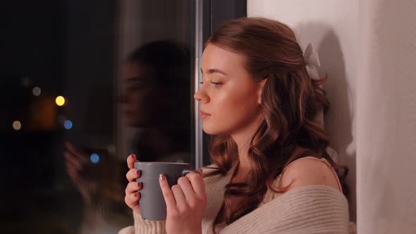 Young Woman Drinking Coffee or Tea at Window