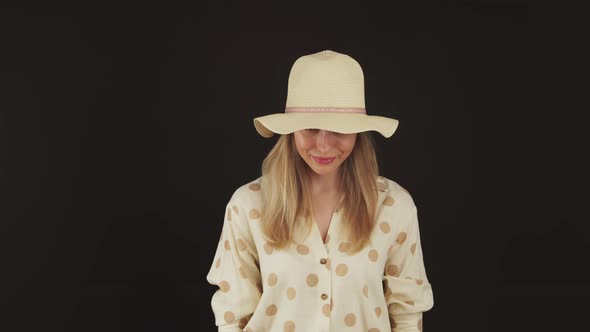 Stunning Blond Caucasian Woman in a Dotted Shirt and a Hat Slowly Looking Up and Gazing at Camera