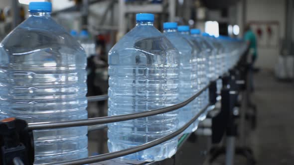 Blue five-liter bottles go on the conveyor in the shop for the production of drinking water