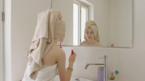 Teenage girl applying mascara in front of the bathroom mirror