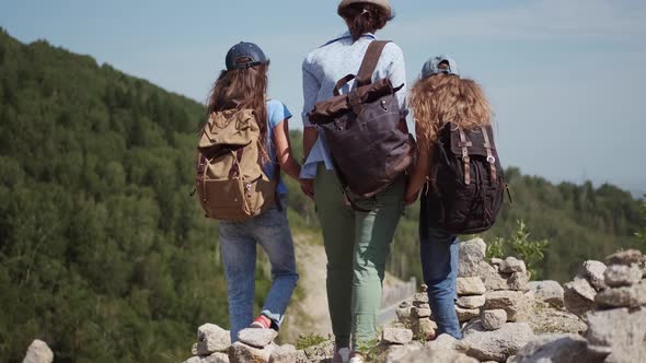 Family of Travelers Walks in the Mountains. Young Woman Leads Her Children on a Hike