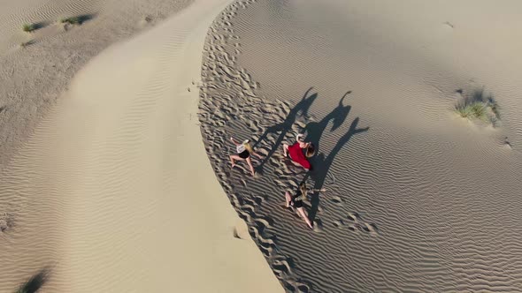 Three Women are Posing and Doing Yoga on Top of a Sand Dune Desert