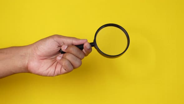 Hand Holding Magnifying Glass Against Yellow Background