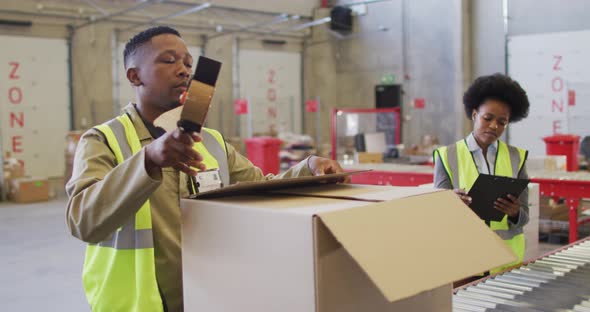 African american male and female workers wearing safety suits and packing boxes in warehouse