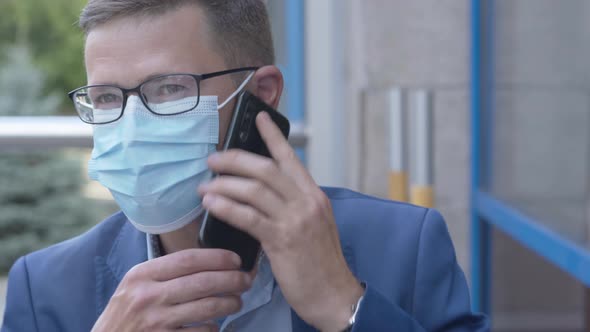 Close-up Portrait of Successful Caucasian Man in Eyeglasses and Face Mask Talking on the Phone