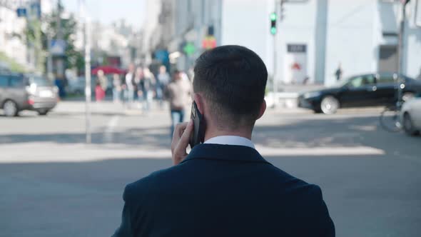 Rear View of Male Businessman Talking on the Phone While Walking in the City Street