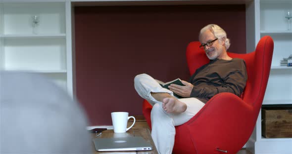 Senior man reading a book in living room 4k