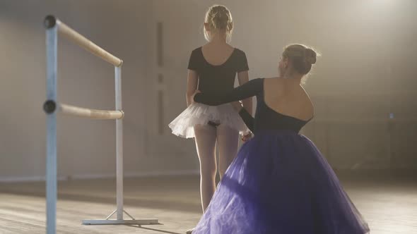 Back View of Slim Ballet Teacher Adjusting Tutu of Little Student in Dancing Studio Sitting on Floor