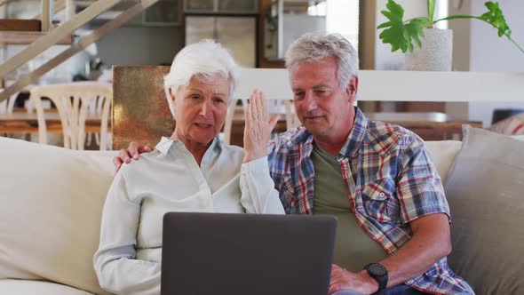 Senior caucasian couple having a video chat on laptop while sitting on couch at home