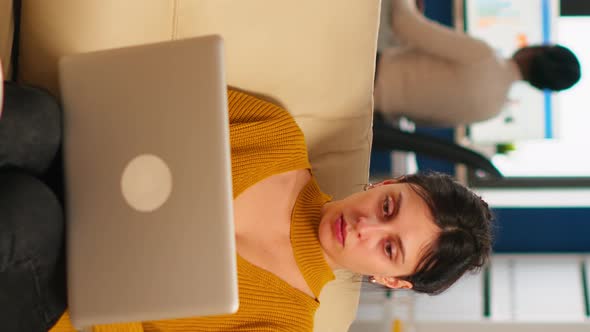 Businesswoman Sitting on Couch Holding Laptop Smiling at Camera