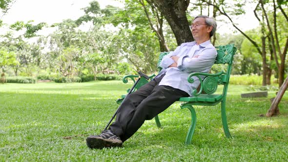 An old Asian man sits comfortably in a green park.