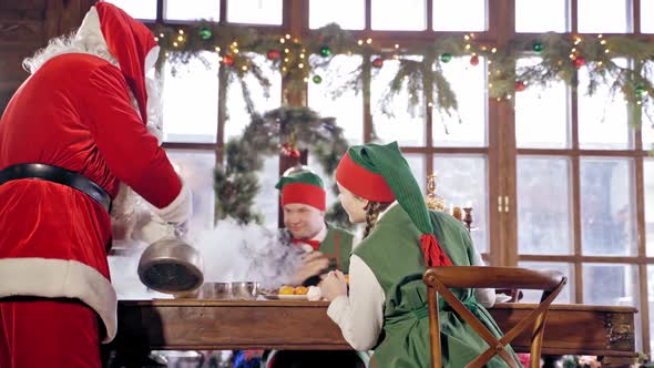 Santa Claus is pouring hot tea to the cups in specially decorated room.