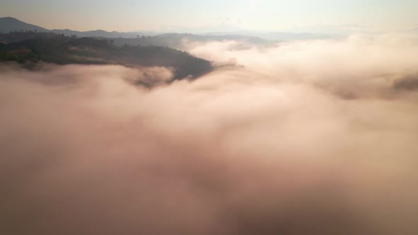 4K aerial view over mountain at sunrise in heavy fog. golden morning sunlight