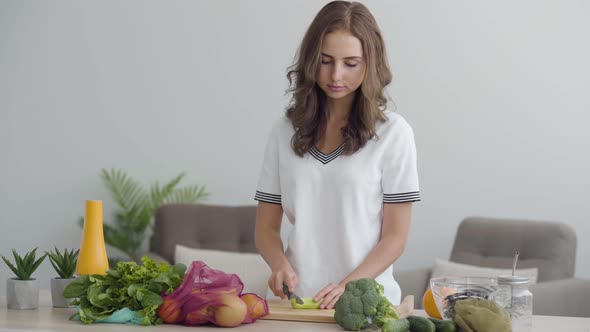 Young Slim Woman Slicing Vegetables with the Sharp Knife at the Table in the Kitchen