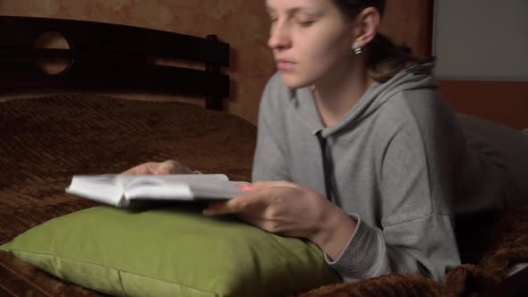 Beautiful Girl Reads a Book Comfortably While Lying in Bed