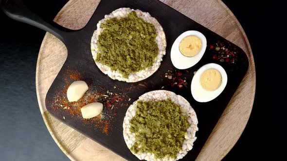 Rice Cake Toasts with Spreading Green Pesto Sauce and Boiled Eggs Rotate Slowly on Cutting Board