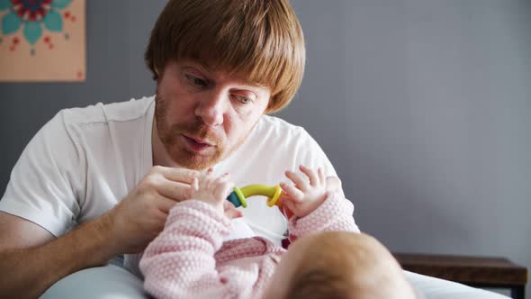 Caressing Dad with Toy Grimacing and Playing with Lying Baby