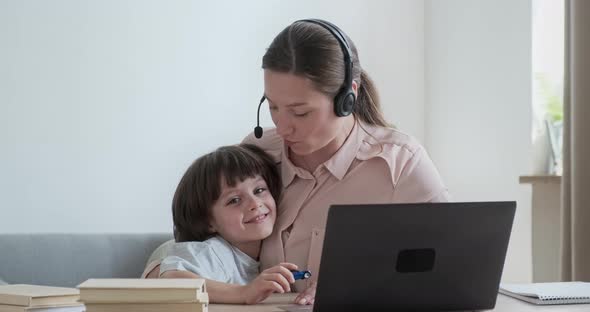 Mother Businesswoman Working Remotely From Home on Video Conference When Cute Boy Rushes Up and