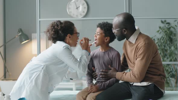 Female Doctor Checking Throat of African American Boy with Flashlight