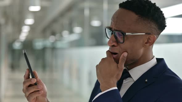 Portrait of African Businessman Reacting To Loss on Smartphone 